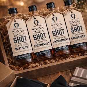 Puede incluir: Cuatro botellas de licor en miniatura con etiquetas que dicen "Wanna Take a Shot" para una boda. Las botellas están en una caja de madera con una pajarita y una caja de regalo. Las etiquetas incluyen la fecha 14 de noviembre de 2026.