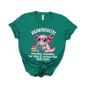 Puede incluir: Una camiseta verde azulado con un gr&aacute;fico de un ajolote rosa con gafas y leyendo un libro. El texto "READSOLOTL" est&aacute; encima del ajolote, y "Murphey Academy for Kind & Curious Kids 2025-2026" est&aacute; debajo.