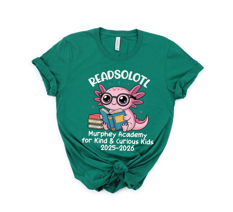 Puede incluir: Una camiseta verde azulado con un gr&aacute;fico de un ajolote rosa con gafas y leyendo un libro. El texto "READSOLOTL" est&aacute; encima del ajolote, y "Murphey Academy for Kind & Curious Kids 2025-2026" est&aacute; debajo.