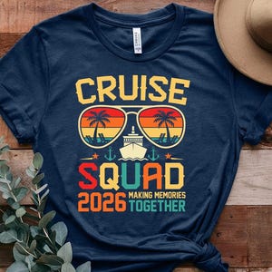 May include: Navy blue t-shirt with a graphic design featuring the words "CRUISE SQUAD 2026" in yellow, orange, and red. The design includes sunglasses with palm trees, a cruise ship, and the phrase "MAKING MEMORIES TOGETHER."