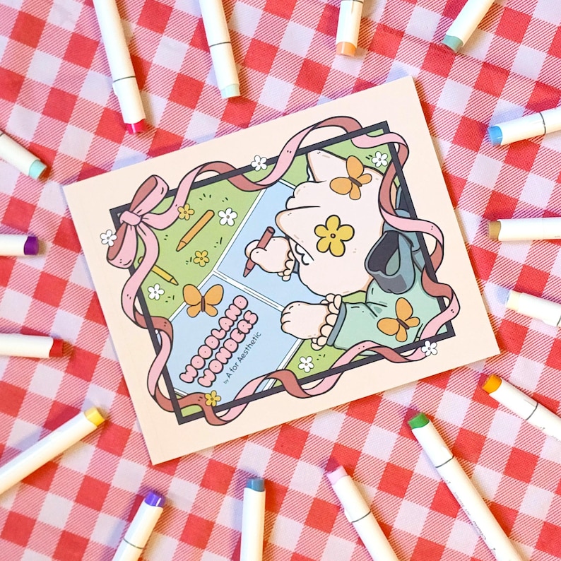 Op de afbeelding: Een vierkante kunstdruk met de woorden "Woodland Wonders" en een cartoonillustratie. De print is omgeven door witte stiften met gekleurde punten, tegen een rood-wit geruite achtergrond.