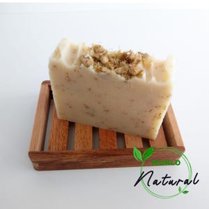 May include: A white bar of soap with dried flowers on top, sitting on a wooden soap dish. The soap dish has the words "Mundo Natural" printed on it.