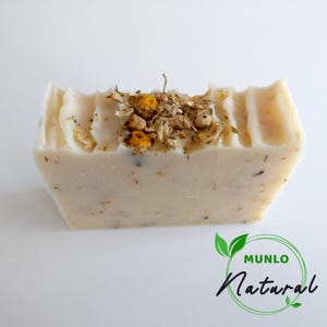 May include: A white bar of soap with dried chamomile flowers on top. The soap is labelled "MUNLO Natural".