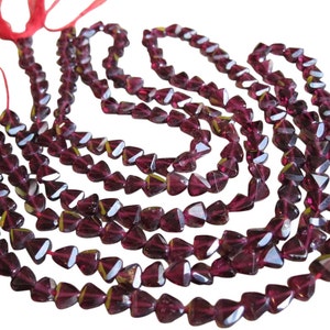 May include: A strand of deep red gemstone beads, each bead is faceted and shaped like a triangle. The beads are strung on a red thread and are ready to be used for jewelry making.