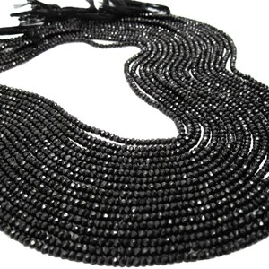 May include: A strand of black faceted gemstone beads. The beads are small and uniform in size, and they are strung on a thin cord. The strand is long and can be used to make jewelry or other crafts.