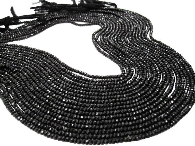 May include: A strand of black faceted gemstone beads. The beads are small and uniform in size, and they are strung on a thin cord. The strand is long and can be used to make jewelry or other crafts.