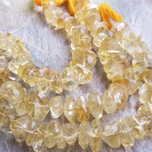 May include: Strands of faceted, golden-yellow citrine gemstone beads. The beads are strung together, with a tassel of yellow thread at the end. The gemstones have a rough, irregular shape and a translucent quality.