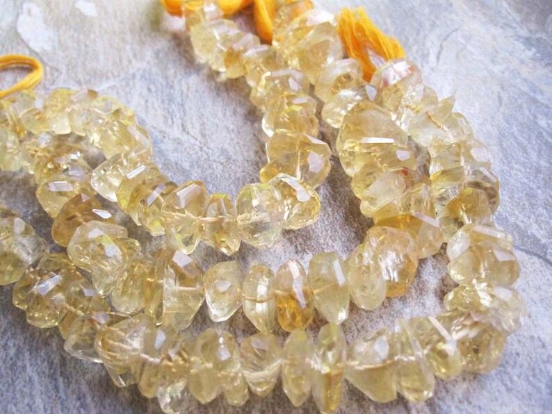 May include: Strands of faceted, golden-yellow citrine gemstone beads. The beads are strung together, with a tassel of yellow thread at the end. The gemstones have a rough, irregular shape and a translucent quality.