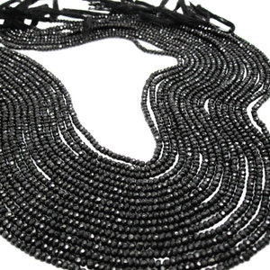May include: A strand of black gemstone beads, faceted and round, strung together in a long necklace. The beads are arranged in a loose, flowing pattern, creating a delicate and elegant look.