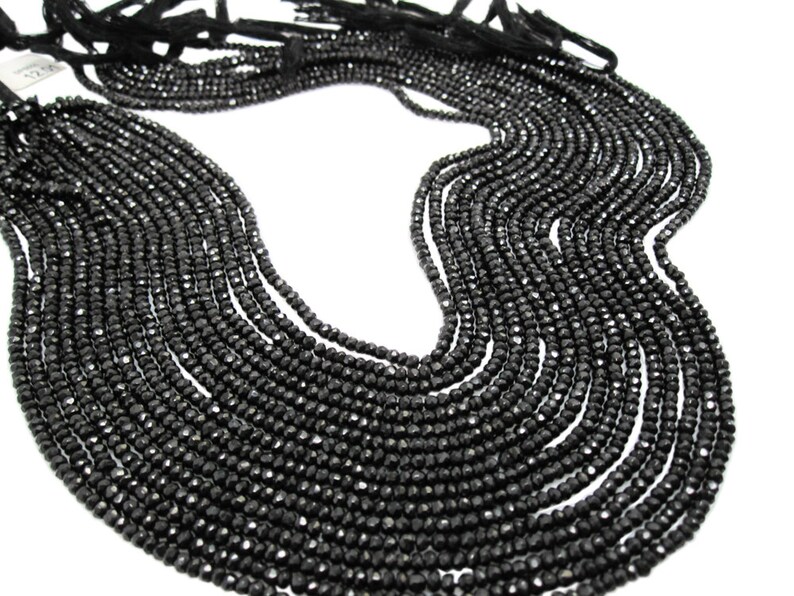 May include: A strand of black gemstone beads, faceted and round, strung together in a long necklace. The beads are arranged in a loose, flowing pattern, creating a delicate and elegant look.