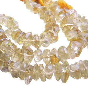 May include: Strands of faceted, light yellow citrine gemstone beads. The beads are irregular in shape and strung on a yellow cord. The gemstones have a translucent quality, reflecting light. The background is white.