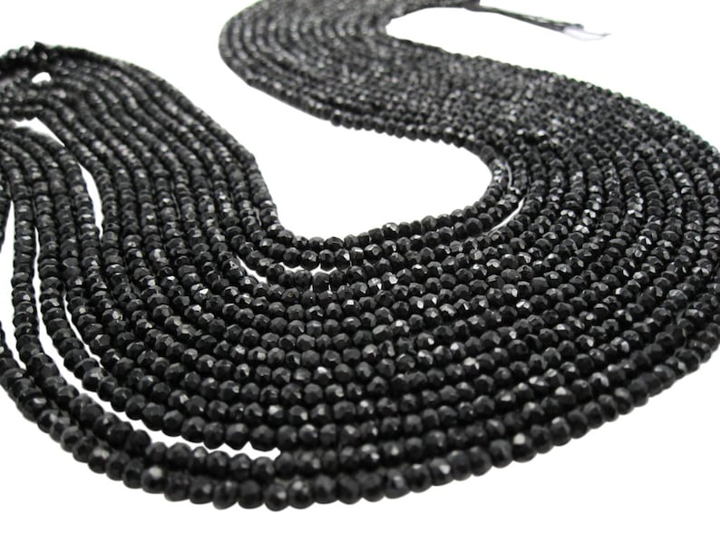 May include: A strand of black faceted gemstone beads. The beads are round and have a smooth, polished finish.