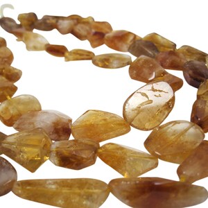 May include: A strand of golden citrine gemstone beads. The beads are faceted and have a natural, irregular shape. The beads are strung on a clear cord.