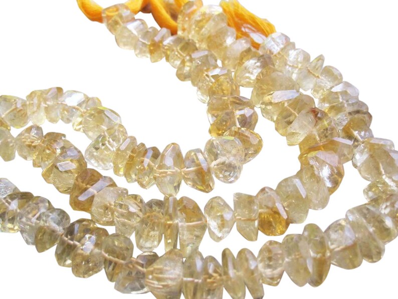 May include: Strands of faceted, irregular-shaped citrine gemstone beads. The beads are a translucent yellow-orange color, strung together with yellow thread. The background is white.