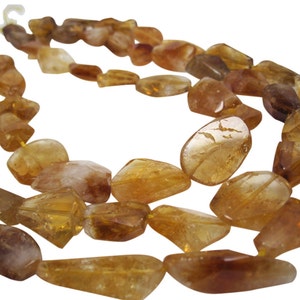 May include: A strand of golden citrine gemstone beads. The beads are faceted and have a natural, irregular shape. The beads are strung on a clear thread.