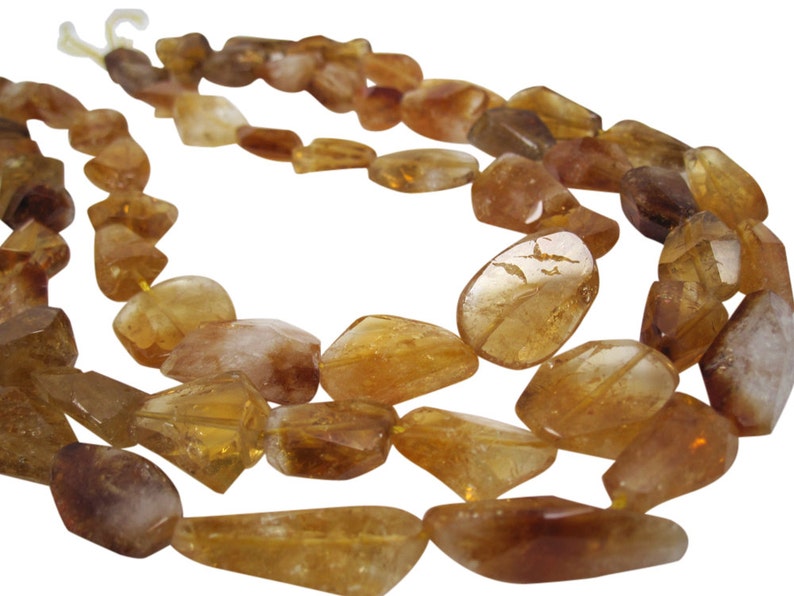 May include: A strand of golden citrine gemstone beads. The beads are faceted and have a natural, irregular shape. The beads are strung on a clear thread.