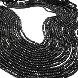 May include: A strand of black faceted gemstone beads. The beads are small and round, and they are strung together on a thin thread. The beads are arranged in a loose, flowing pattern.