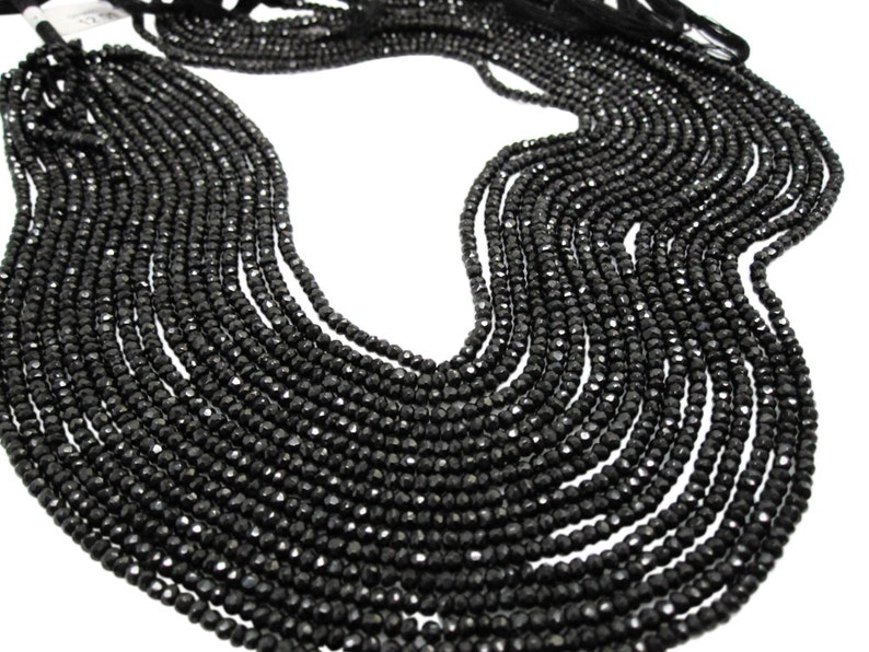 May include: A strand of black faceted gemstone beads. The beads are small and round, and they are strung together on a thin thread. The beads are arranged in a loose, flowing pattern.