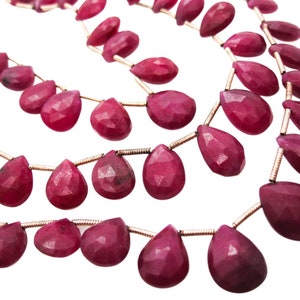 May include: A strand of ruby red gemstone beads in a teardrop shape. The beads are strung on a thin gold wire.