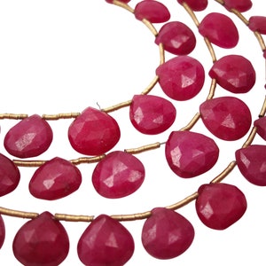May include: A strand of pink gemstone beads in a teardrop shape. The beads are strung on gold wire.