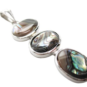 Pode incluir: Um pingente de prata com tr&ecirc;s conchas de abalone ovais. As conchas exibem cores iridescentes de verde, azul e marrom. O pingente tem um design simples e elegante.