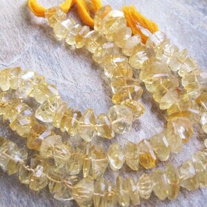 May include: Strands of faceted, golden-yellow citrine gemstone beads. The beads are strung together with yellow thread, and the cut of the stones creates a sparkling effect. The gemstones are a light, translucent yellow color.