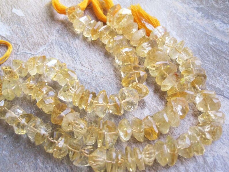 May include: Strands of faceted, golden-yellow citrine gemstone beads. The beads are strung together with yellow thread, and the cut of the stones creates a sparkling effect. The gemstones are a light, translucent yellow color.