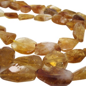 May include: A strand of golden citrine gemstone beads, each bead is faceted and has a unique shape. The beads are strung on a yellow thread.
