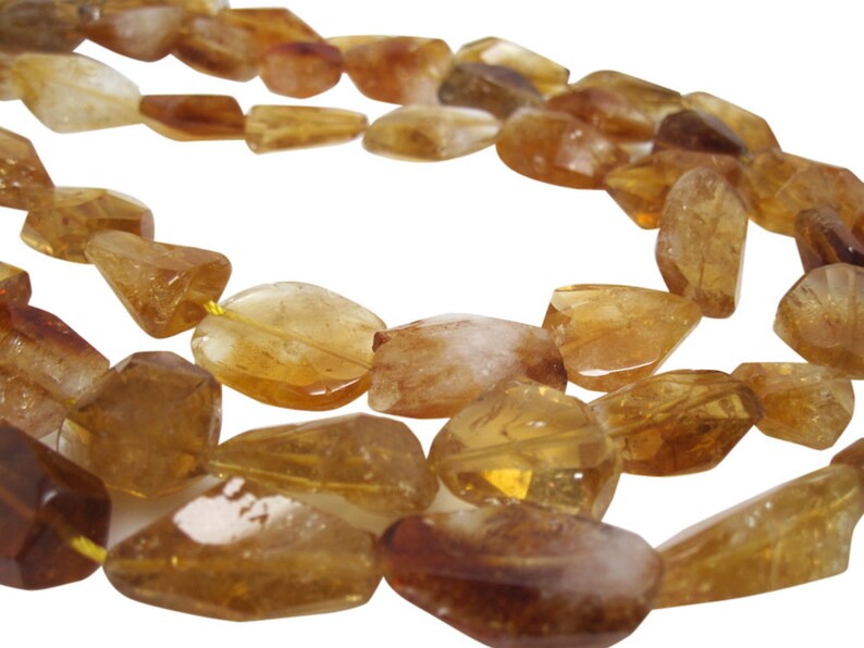 May include: A strand of golden citrine gemstone beads, each bead is faceted and has a unique shape. The beads are strung on a yellow thread.