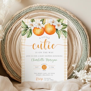 Peut inclure: Faire-part de baby shower avec un motif floral orange et blanc. L'invitation pr&eacute;sente le texte "A Little Cutie Is On The Way" et les d&eacute;tails de l'&eacute;v&eacute;nement. L'invitation est plac&eacute;e sur un fond tiss&eacute; avec un motif vichy.