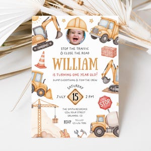 May include: A personalized birthday invitation with a construction theme. The design features illustrations of construction vehicles, a baby wearing a construction hat, and the text "William is turning one year old!" The invitation is in shades of beige, yellow, and brown.