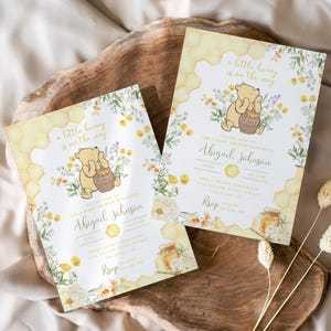 May include: Two baby shower invitations with a Winnie the Pooh theme. The invitations feature a cartoon bear holding a honey pot, surrounded by floral and honeycomb designs. The text reads "a little hunny is on the way."
