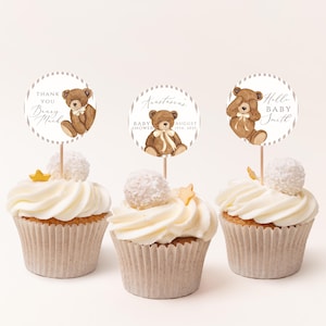 Op de afbeelding: Drie cupcakes met witte glazuur, elk bekroond met een decoratieve ronde topper met een bruine teddybeer illustratie. De toppers hebben de tekst "Thank You Beary Much", "Anastasia's Baby Shower August 15th, 2023" en "Hello Baby Smith".