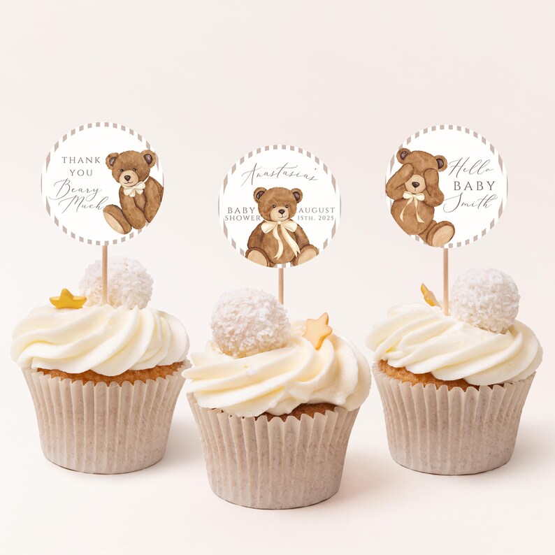 Op de afbeelding: Drie cupcakes met witte glazuur, elk bekroond met een decoratieve ronde topper met een bruine teddybeer illustratie. De toppers hebben de tekst "Thank You Beary Much", "Anastasia's Baby Shower August 15th, 2023" en "Hello Baby Smith".