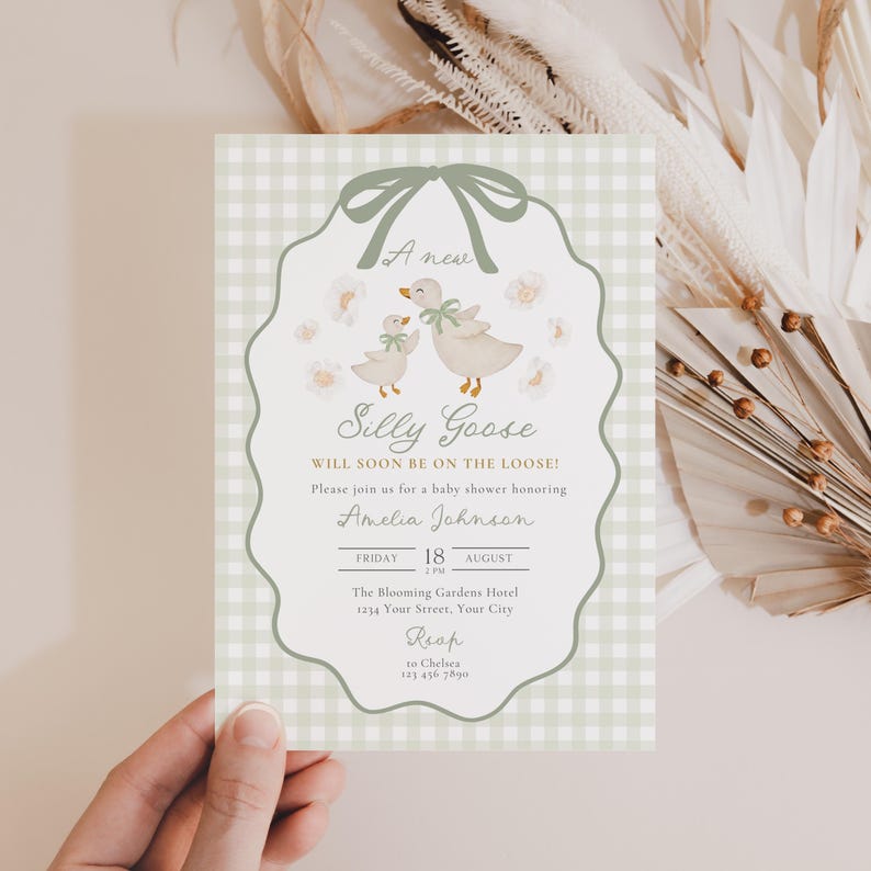 May include: A baby shower invitation with a whimsical design. The invitation features a light green gingham background and a scalloped border. The text reads "Silly Goose" with illustrations of geese and flowers. The invitation is held by a hand.