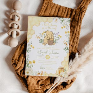 May include: A baby shower invitation featuring Winnie the Pooh with the text "A little hunny is on the way." The invitation includes the name "Abigail Johnson," date, time, and RSVP information. The design incorporates floral and honeycomb elements.
