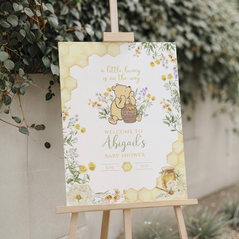 Puede incluir: Un letrero de bienvenida para baby shower sobre un caballete. El letrero presenta una ilustraci&oacute;n de Winnie the Pooh con el texto "a little hunny is on the way" y "Welcome to Abigail's Baby Shower". El dise&ntilde;o incluye elementos florales y de panal.