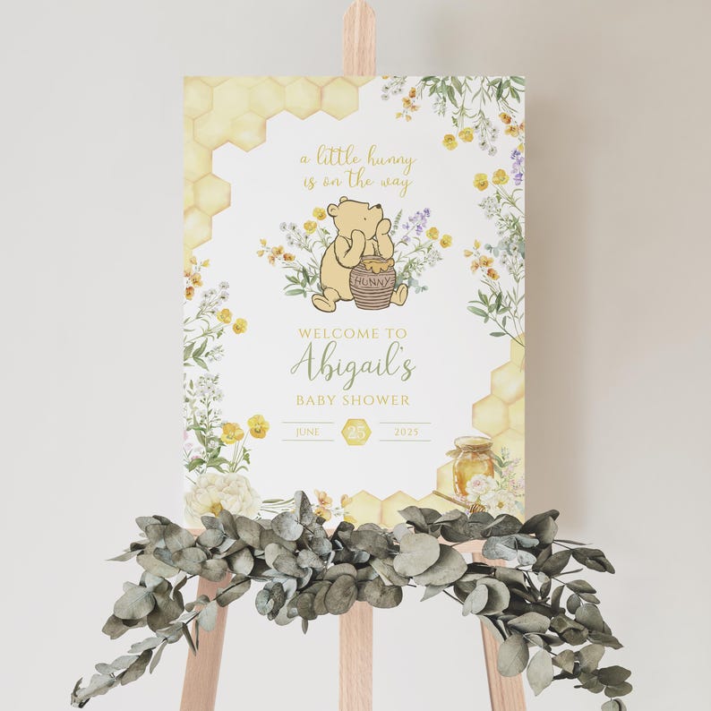 Puede incluir: Un letrero de bienvenida para baby shower con Winnie the Pooh y el texto "a little hunny is on the way." El letrero incluye dise&ntilde;os florales y de panal, con "Abigail's" y la fecha 25 de junio de 2025.