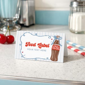 May include: A folded food label with a retro design. The label features a brown soda bottle illustration with a blue bow, the word "Cola", and the text "Food Label YOUR TEXT HERE" in red and black. The background has blue and white stripes.