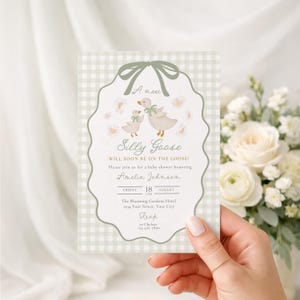 May include: A baby shower invitation with a whimsical design. The invitation features a light green gingham background and a scalloped border. The text reads "A new Silly Goose" with details for the event. The invitation is held by a person.