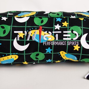 May include: Black crossbody bag with a green, yellow, and blue alien and moon pattern. The bag has the text "TWISTED PERFORMANCE SPIKES" printed on the front.