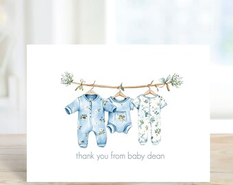 May include: A thank you card with a watercolor illustration of three baby onesies hanging on a branch. The onesies are blue with white floral patterns. The text "thank you from baby dean" is printed below the illustration.