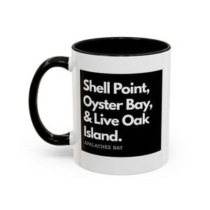 May include: White ceramic mug with a black handle and interior. The mug features the text "Shell Point, Oyster Bay, & Live Oak Island" in white on a black rectangle, with "APALACHEE BAY" below.