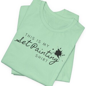 May include: A light green t-shirt with the text "This is my Let Painting Shirt" in black script with a black paint splatter.
