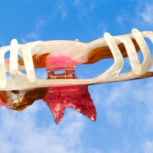 Peut inclure: Une pince &agrave; cheveux en forme de licorne avec un corps blanc nacr&eacute;, une crini&egrave;re brun dor&eacute; et des d&eacute;tails de corne et d'ailes roses. La pince poss&egrave;de un m&eacute;canisme &agrave; ressort m&eacute;tallique au centre et plusieurs griffes incurv&eacute;es pour maintenir les cheveux.