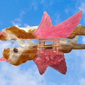 Peut inclure: Une pince &agrave; cheveux en forme de licorne ail&eacute;e avec un corps blanc translucide, une crini&egrave;re brune et des ailes roses. La pince dispose d'un m&eacute;canisme &agrave; ressort m&eacute;tallique central et d'une structure en plastique rose, avec une t&ecirc;te d&eacute;taill&eacute;e.
