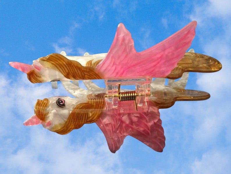 Peut inclure: Une pince &agrave; cheveux en forme de licorne ail&eacute;e avec un corps blanc translucide, une crini&egrave;re brune et des ailes roses. La pince dispose d'un m&eacute;canisme &agrave; ressort m&eacute;tallique central et d'une structure en plastique rose, avec une t&ecirc;te d&eacute;taill&eacute;e.