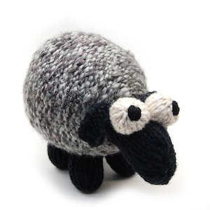 May include: A gray and black knitted sheep toy with large white eyes and a black nose.