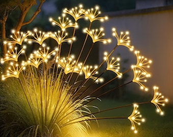 May include: Outdoor decorative lights shaped like illuminated flowers. The lights are warm white and arranged on slender, dark brown stems, creating a glowing display. The lights are set in a grassy area, adding a touch of elegance to the garden.