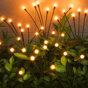 May include: Outdoor decorative lights with warm white LED bulbs on black stems, resembling fireflies. The lights are arranged among green foliage, creating a soft, inviting glow. Ideal for garden or patio decor.